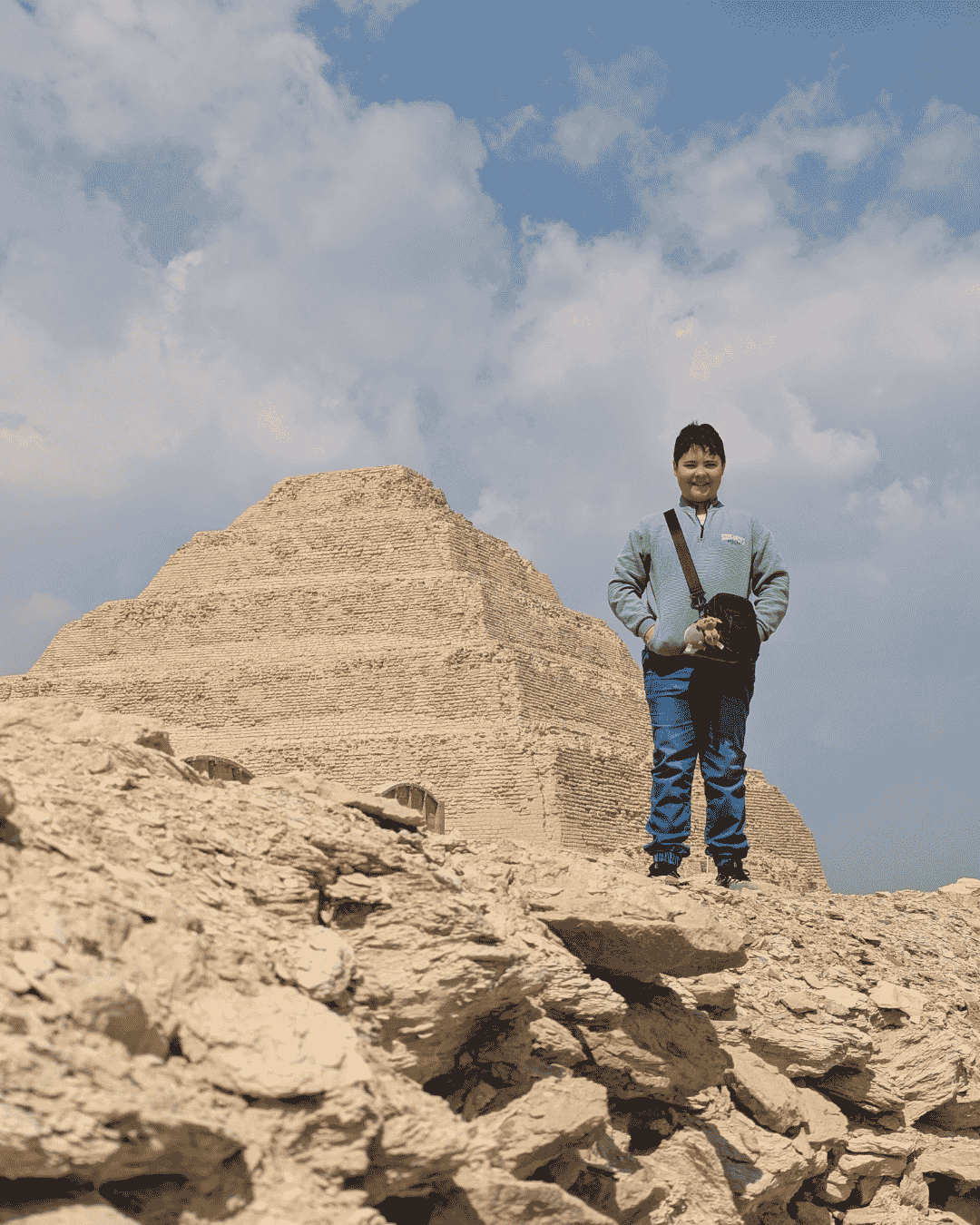 Boy standing on a pile of rocks next to the Djoser Step Pyramid at Saqqara
